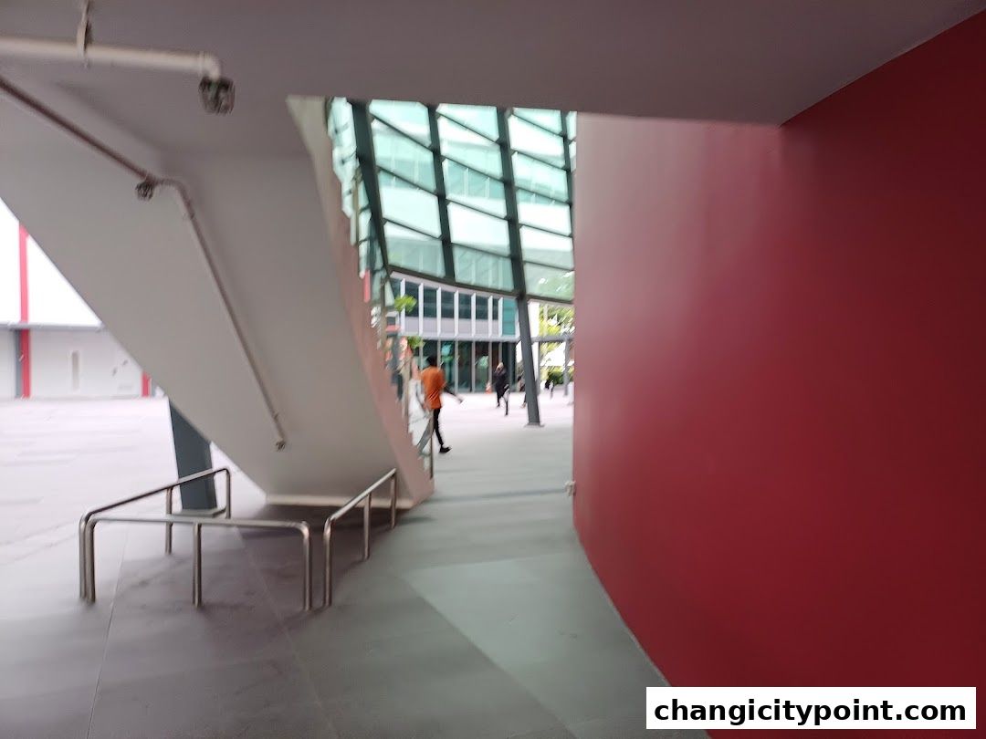 A walkway with a red wall and a modern staircase leading to a building.