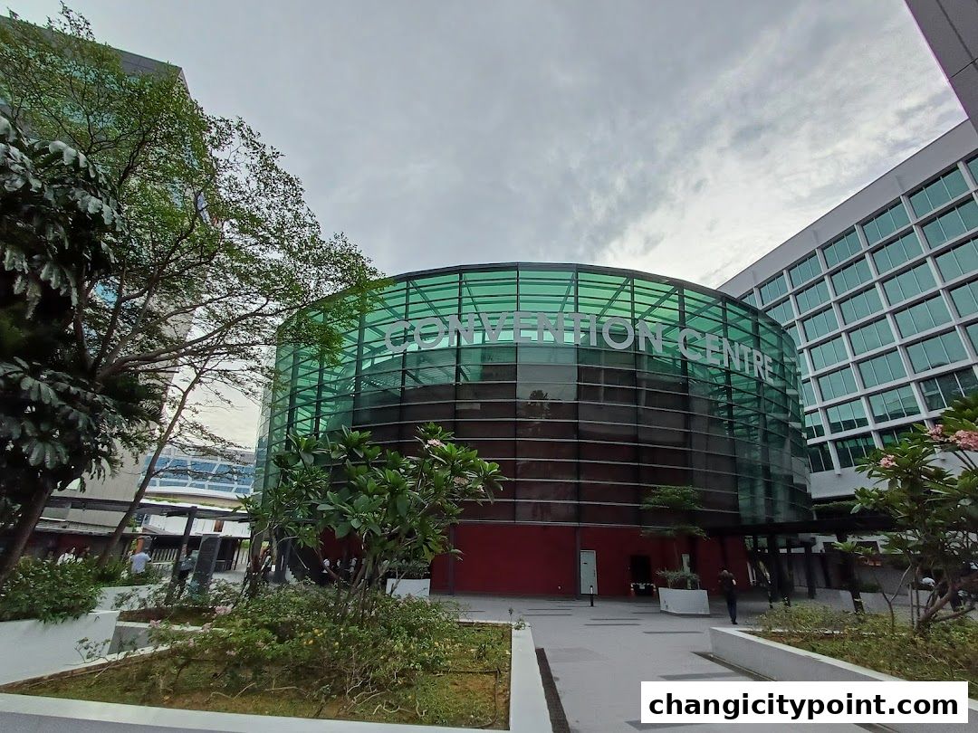 Exterior view of a modern convention centre with green glass facade and surrounding greenery.