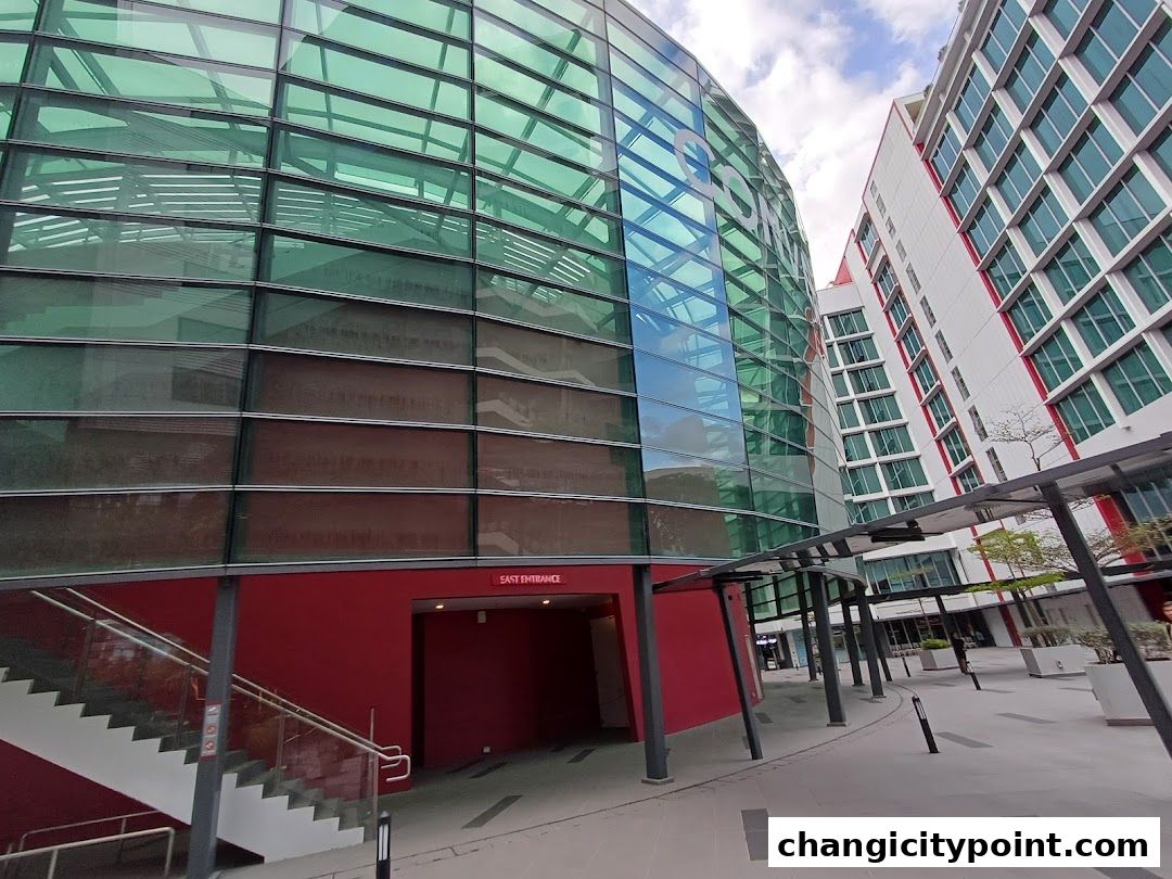Modern building with green glass facade and red entrance, adjacent to a white building.