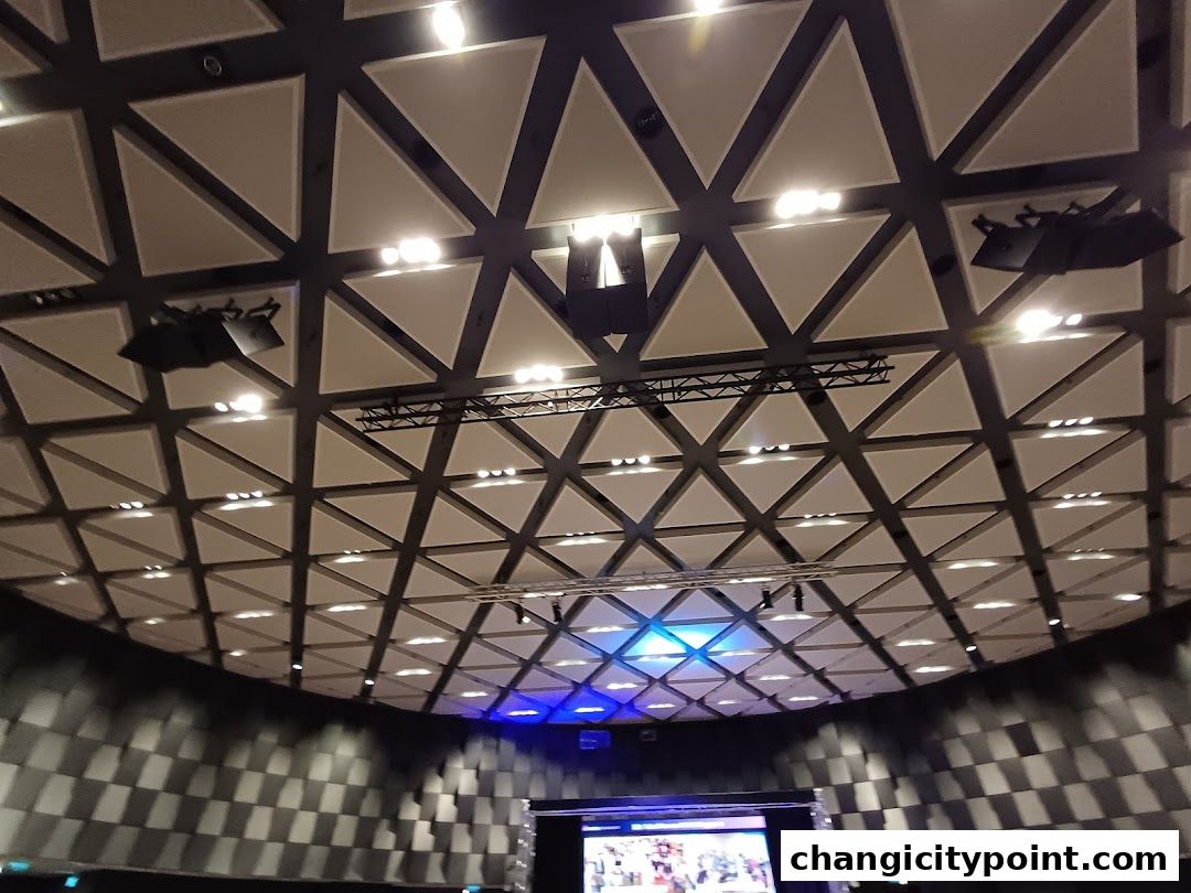 Interior view of a modern venue with a geometric ceiling and stage lighting.