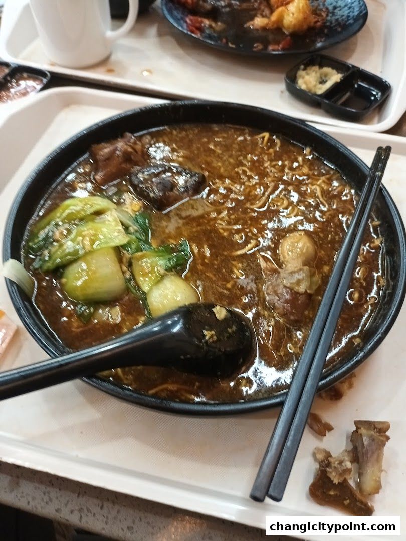 A close-up of a hearty bowl of noodles with meat and vegetables, served with chopsticks.