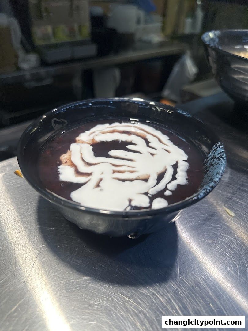 A close-up of a black bowl filled with red bean soup topped with coconut milk.