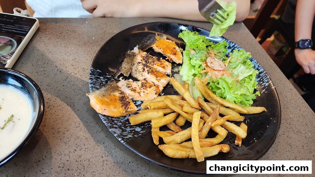 A plate of grilled salmon with fries and salad, next to a bowl of soup.