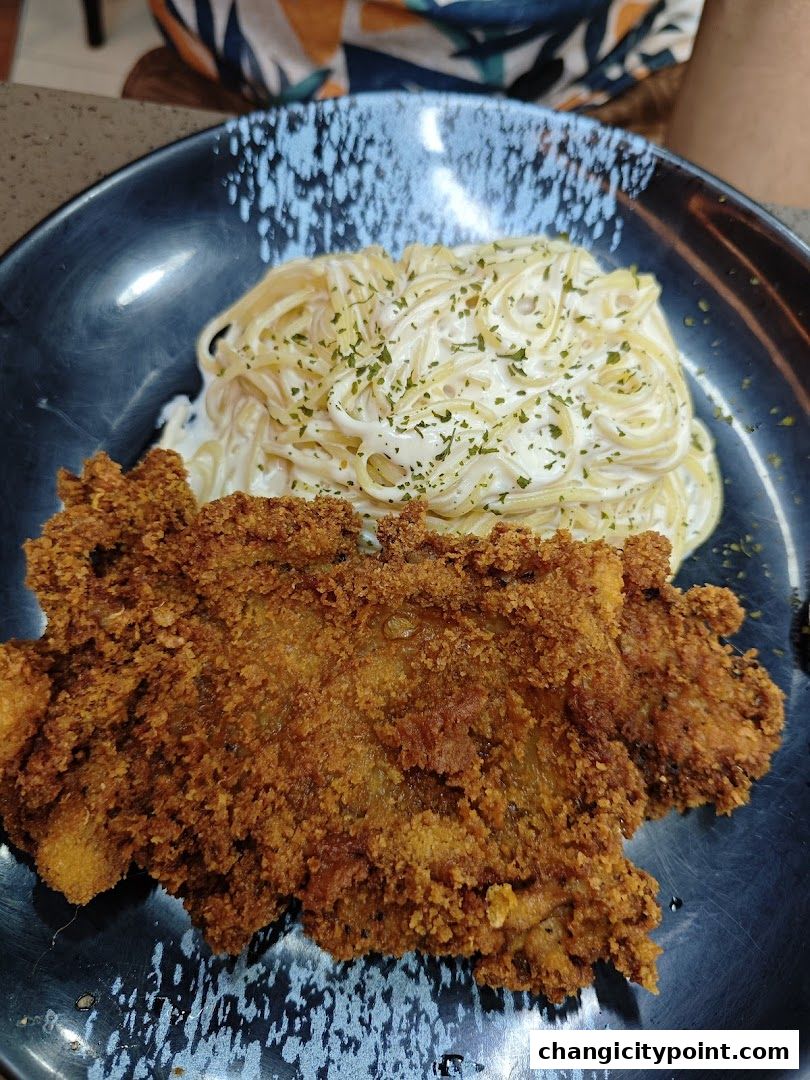 A plate of creamy spaghetti with a crispy fried chicken cutlet, garnished with parsley.