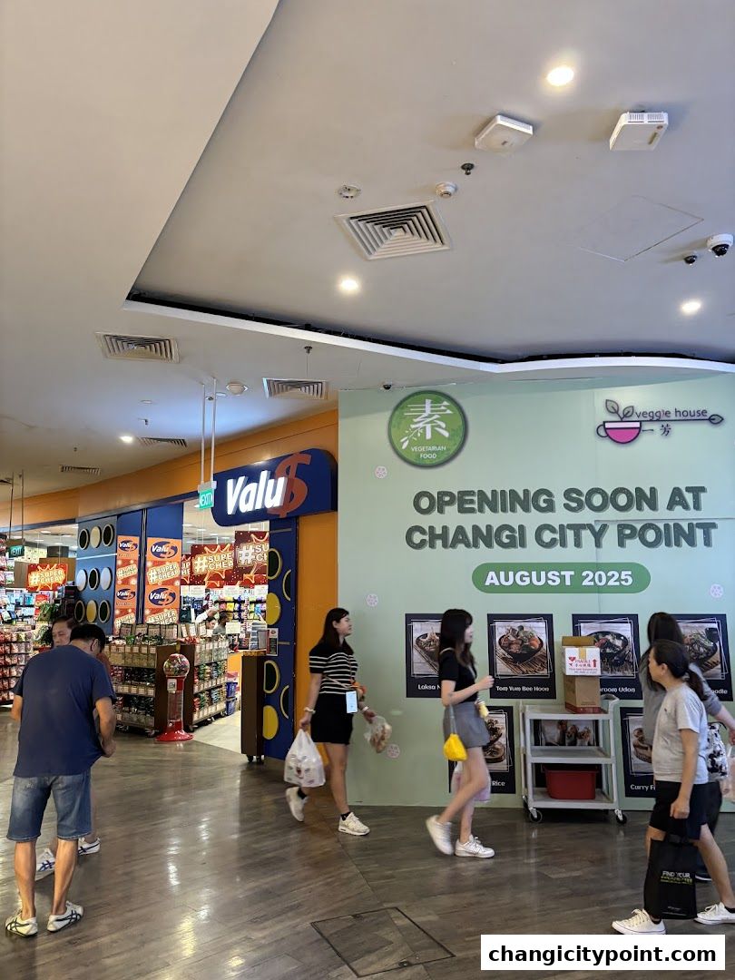 A Valu store entrance and a 'Veggie House' opening soon sign with people walking by.