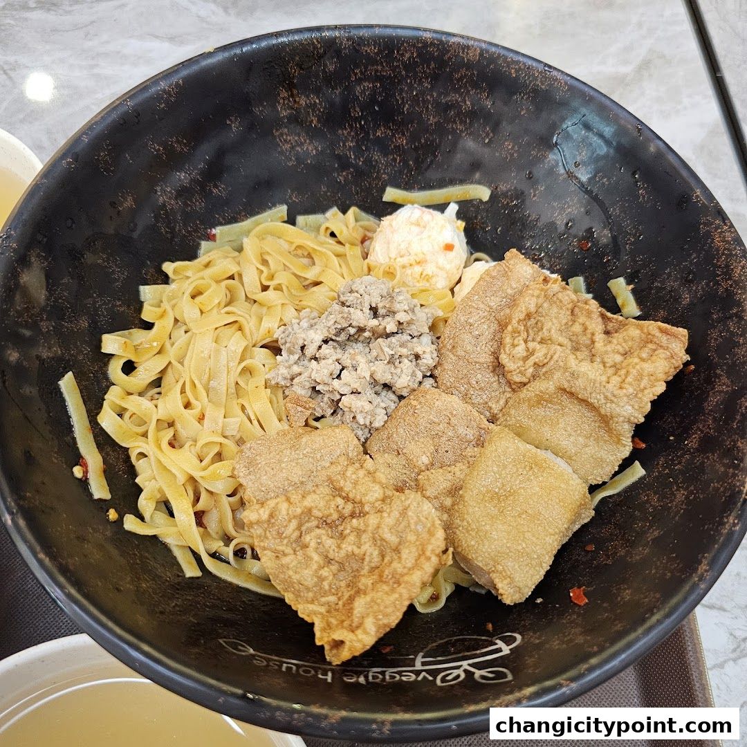 A bowl of noodles with minced meat, fried tofu skin, and a fish ball.