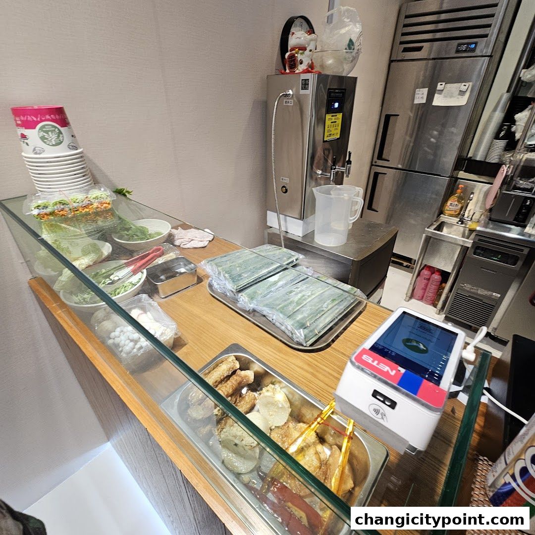 A display counter with fresh ingredients, prepared food, and a payment terminal.