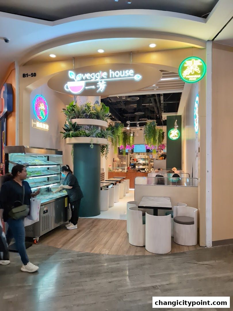 The exterior of Veggie House, a vegetarian food shop, with plants and seating.