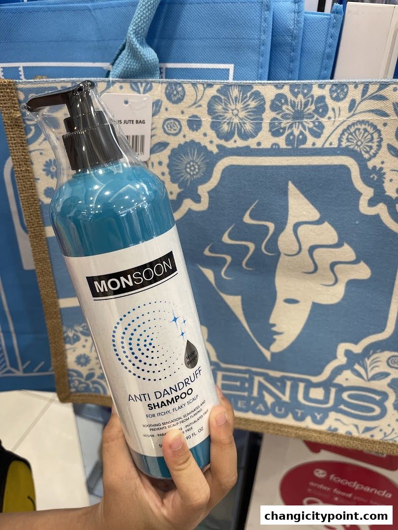 A hand holds a bottle of Monsoon Anti Dandruff Shampoo in front of Venus Beauty bags.