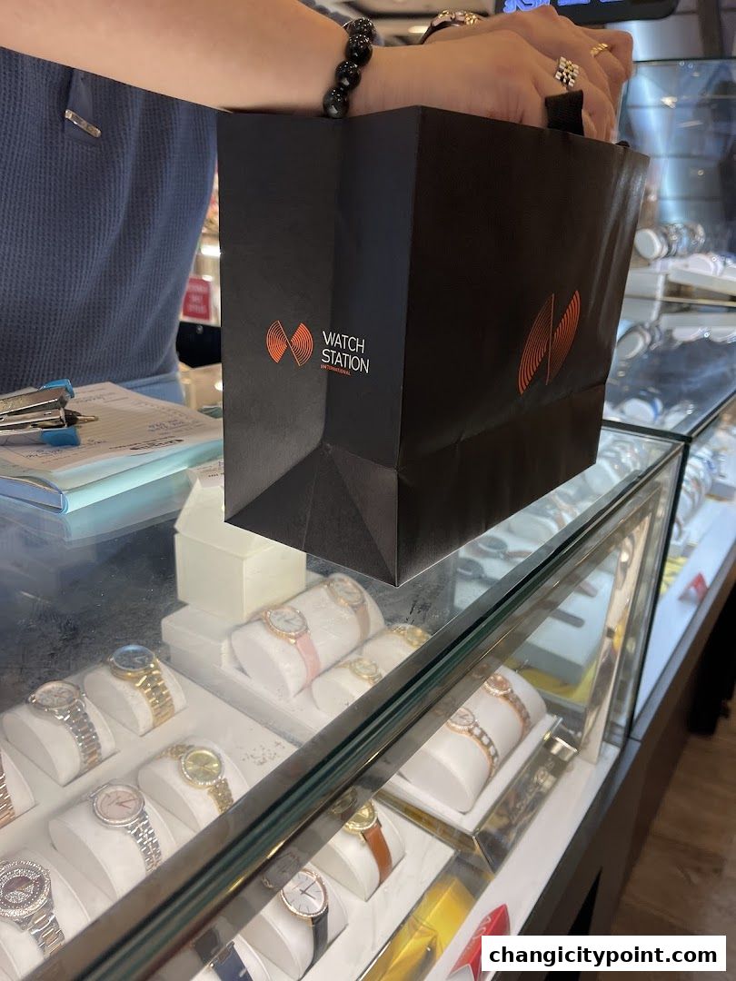 A person holds a Watch Station shopping bag over a display of watches.