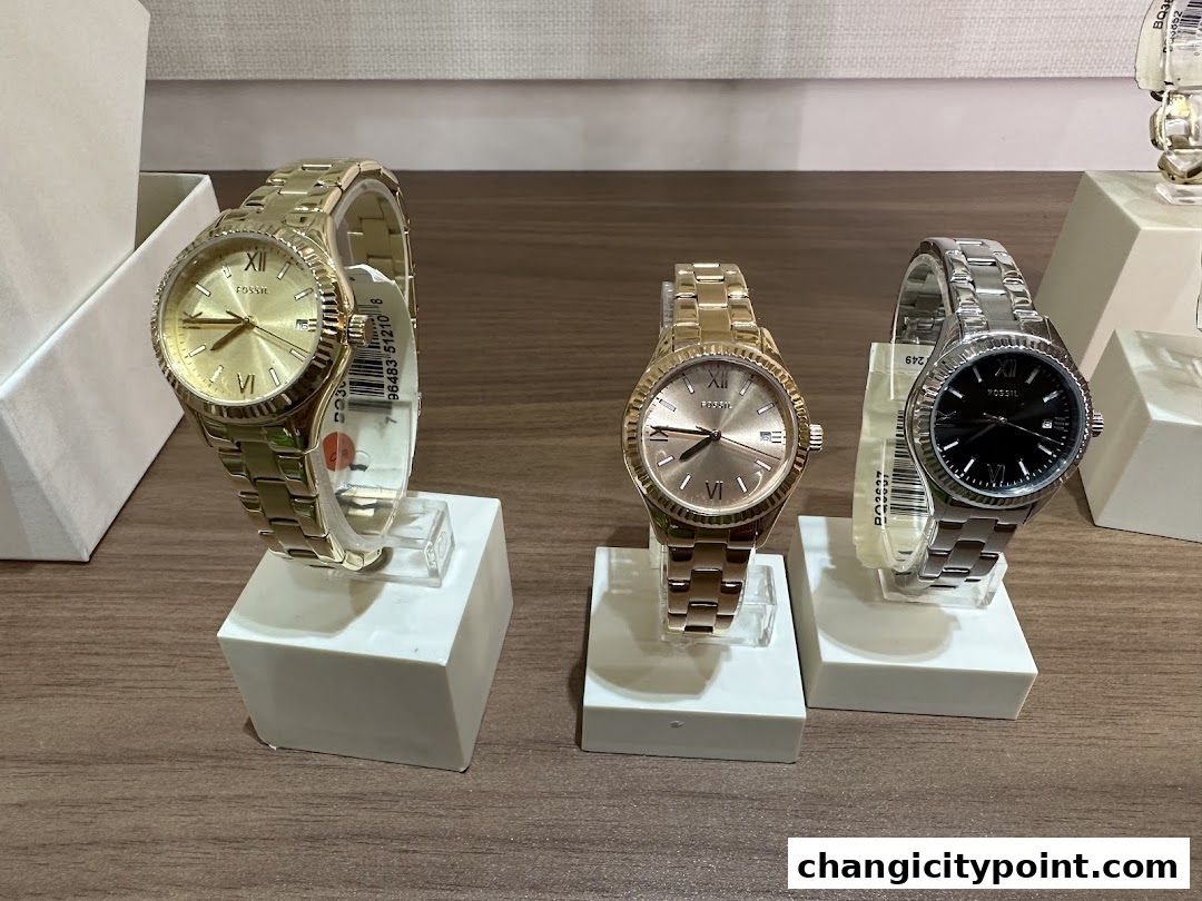 Three Fossil watches displayed on white stands, showcasing gold and silver designs.