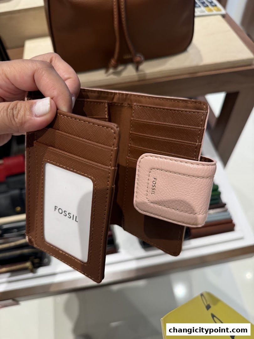 A hand holds open a brown and pink Fossil wallet, showcasing its card slots and branding.