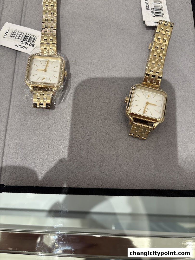 Two elegant gold Fossil watches with square faces displayed on a grey surface.