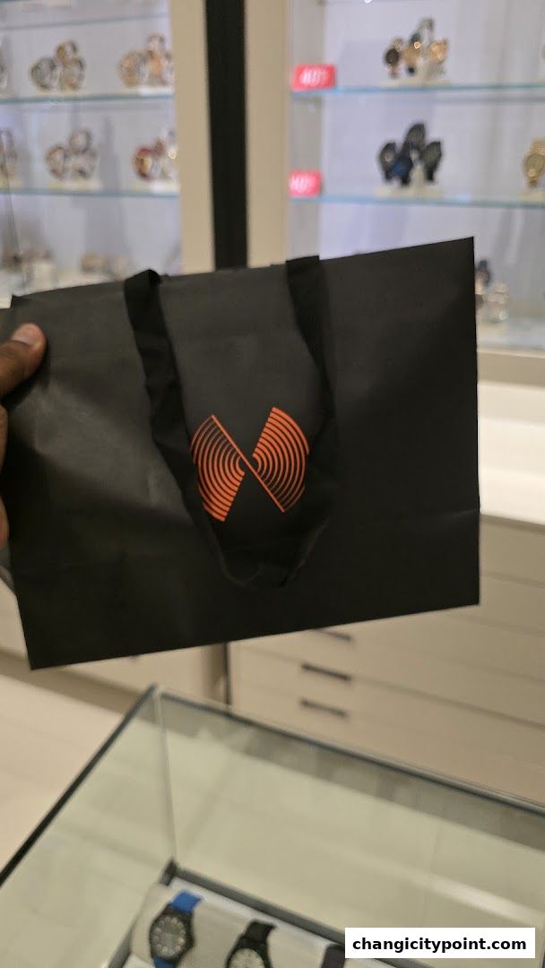 A person holds a black shopping bag with an orange logo inside a watch store.