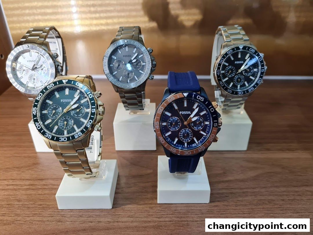 A display of five Fossil watches with various dial colors and strap materials.