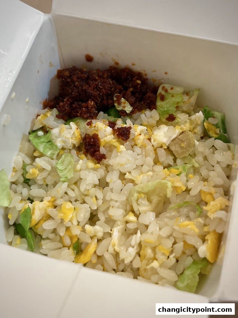 A close-up of a takeaway box filled with fried rice, egg, and vegetables.