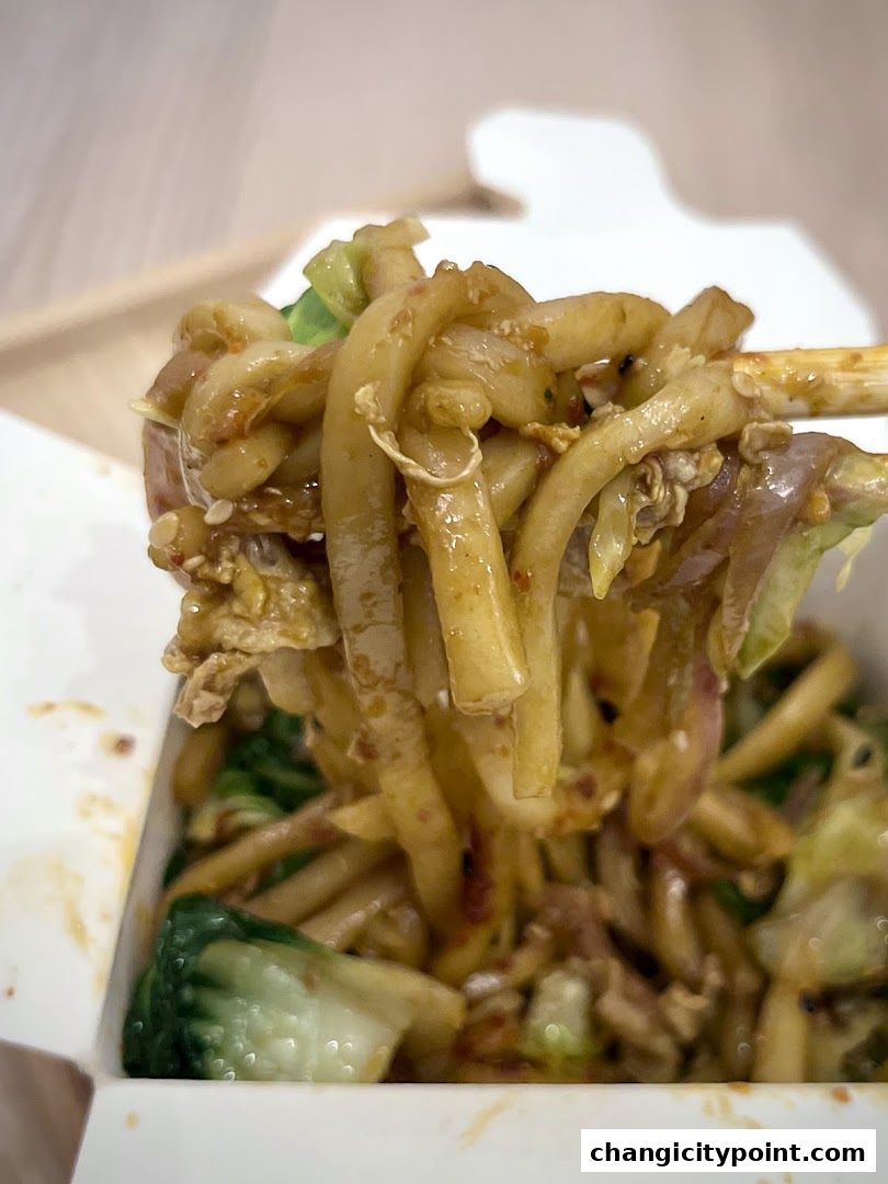 A close-up shot of delicious stir-fried noodles with vegetables being lifted by chopsticks.