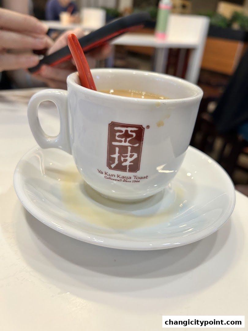 A close-up of a cup of coffee with a red spoon at Ya Kun Kaya Toast.