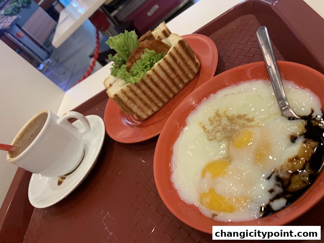 A tray with a cup of coffee, soft-boiled eggs, and a kaya toast sandwich.