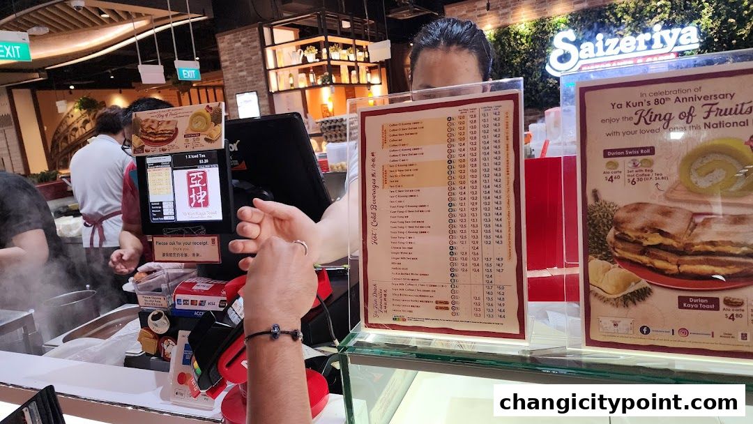 A customer is paying at the counter of Ya Kun Kaya Toast, with menus displayed.