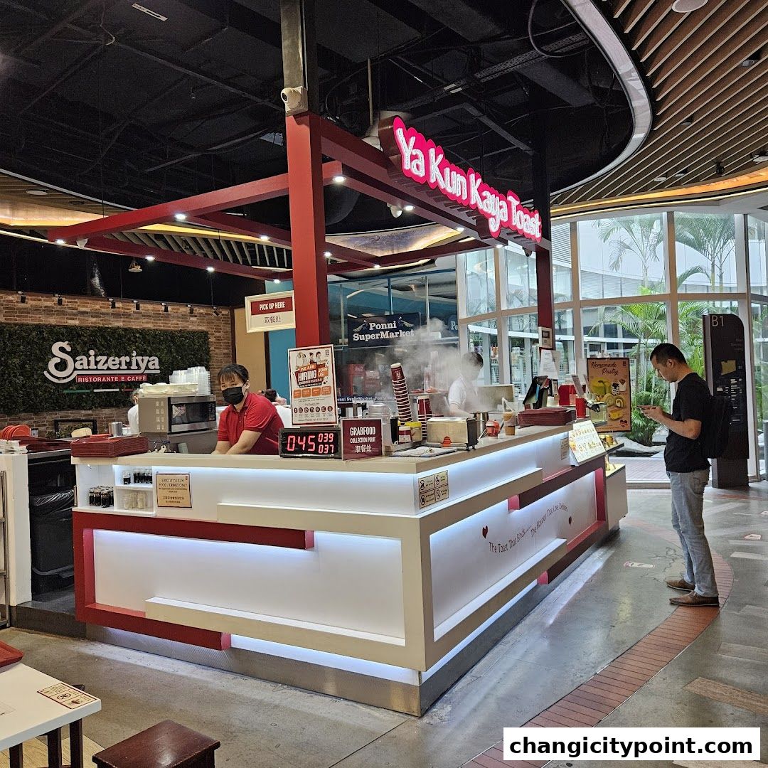 Ya Kun Kaya Toast stall with staff serving customers and a customer looking at their phone.
