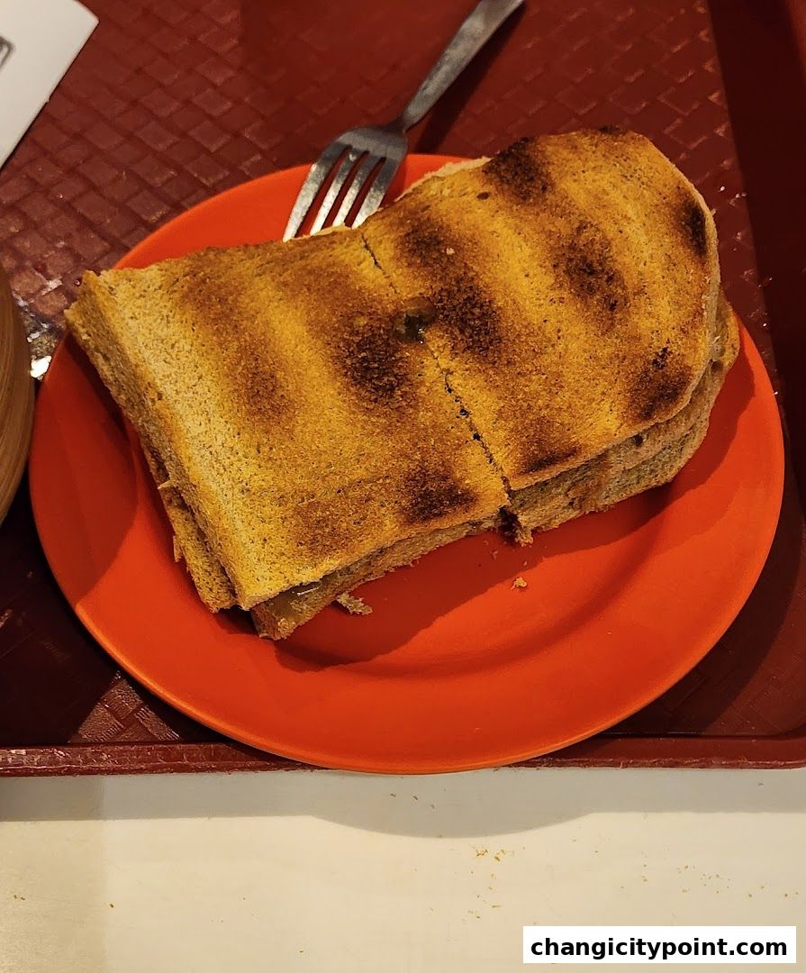 A close-up of a kaya toast sandwich on an orange plate with a fork.