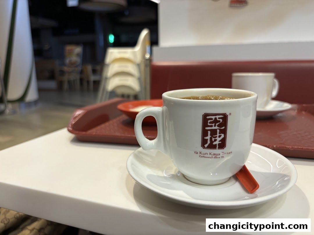 A steaming cup of coffee from Ya Kun Kaya Toast sits on a white table.