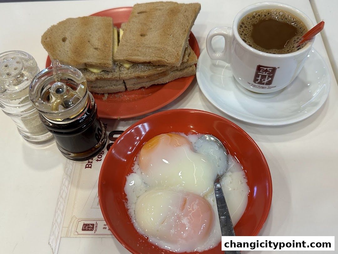 A close-up of a traditional Singaporean breakfast set with kaya toast, soft-boiled eggs, and coffee.