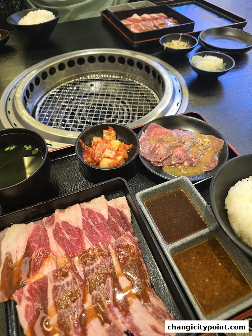 A table set for yakiniku with raw meat, kimchi, rice, soup, and dipping sauces.