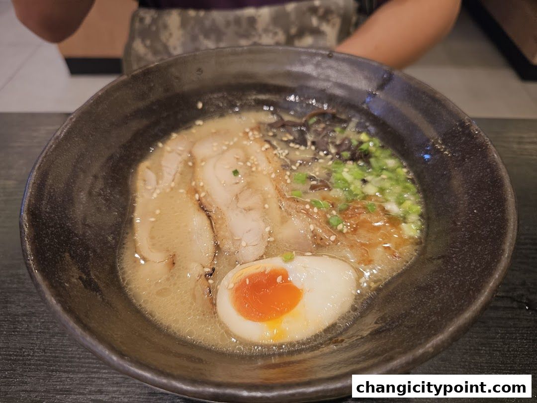 A close-up shot of a steaming bowl of ramen with pork, egg, and green onions.